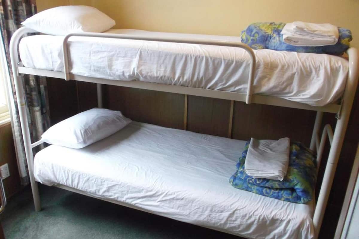 A bunk bed with white bedding and a blue patterned blanket on the lower bunk.