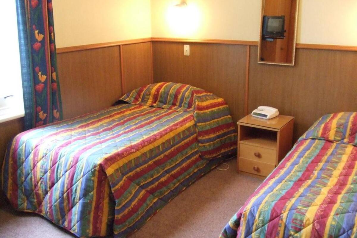 A hotel room with two beds, a bedside table with a phone, and a mirror on the wall.