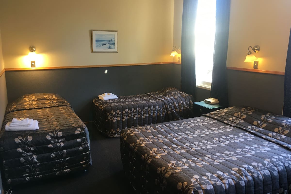 A hotel room with two single beds, a small table, a telephone, and a painting on the wall.