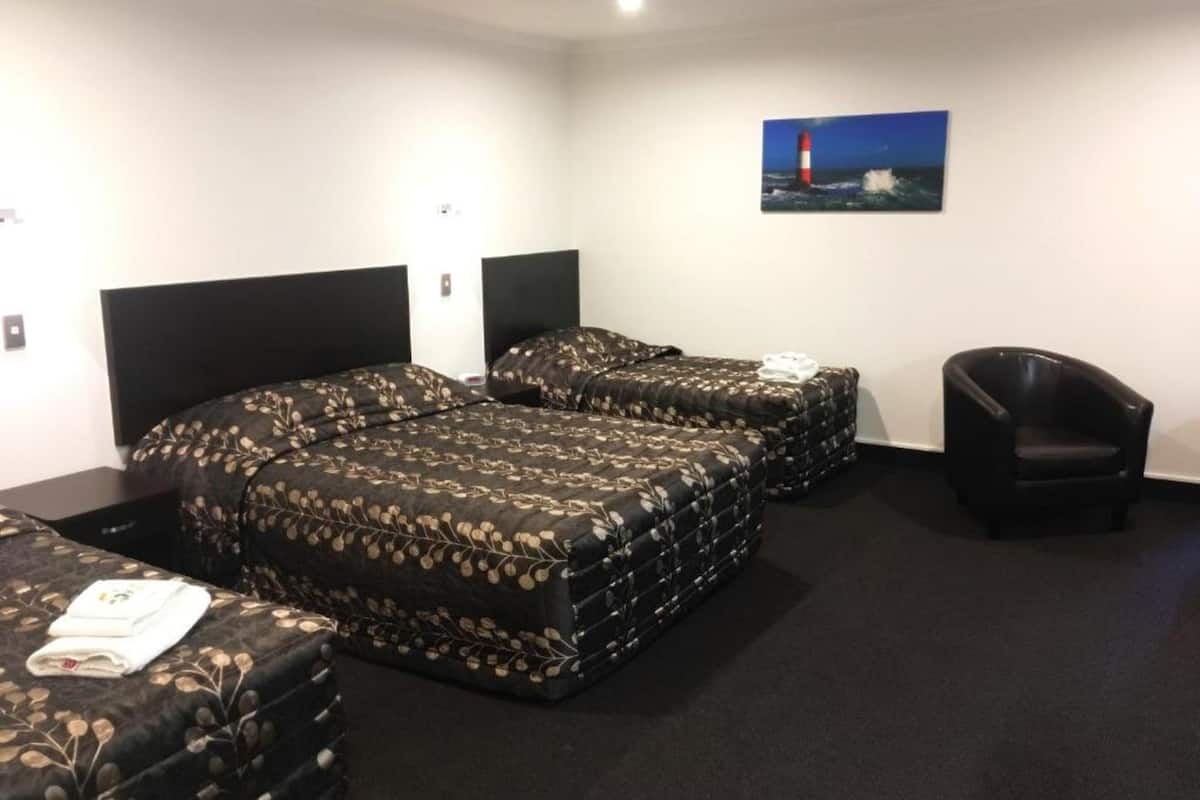 A hotel room with two beds, a chair, and a painting of a lighthouse.