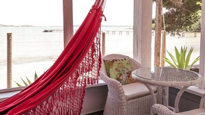 A wicker chair and table set against a window overlooking a beach with a hammock. - Barracuda Resort (Búzios)