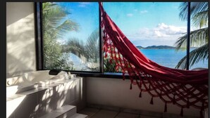 A bathroom with a large window, a bathtub, and a red hammock. - Barracuda Resort (Búzios)