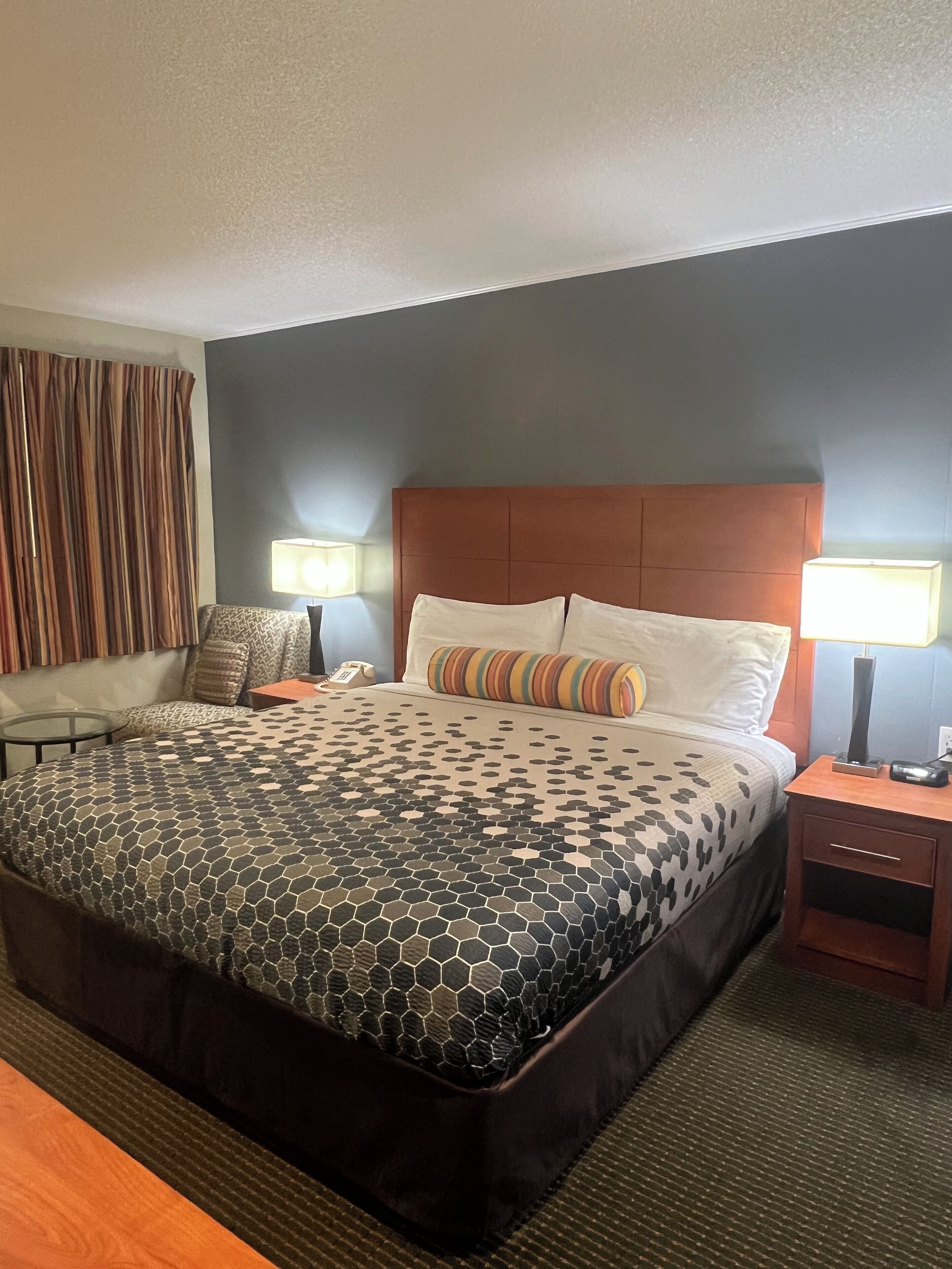 A hotel room with a large bed, two bedside tables, a chair, and a desk.
