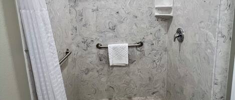 Eine begehbare Dusche mit Marmorboden, einem Handtuchhalter, einem Duschkopf und einer Glasduschtür.