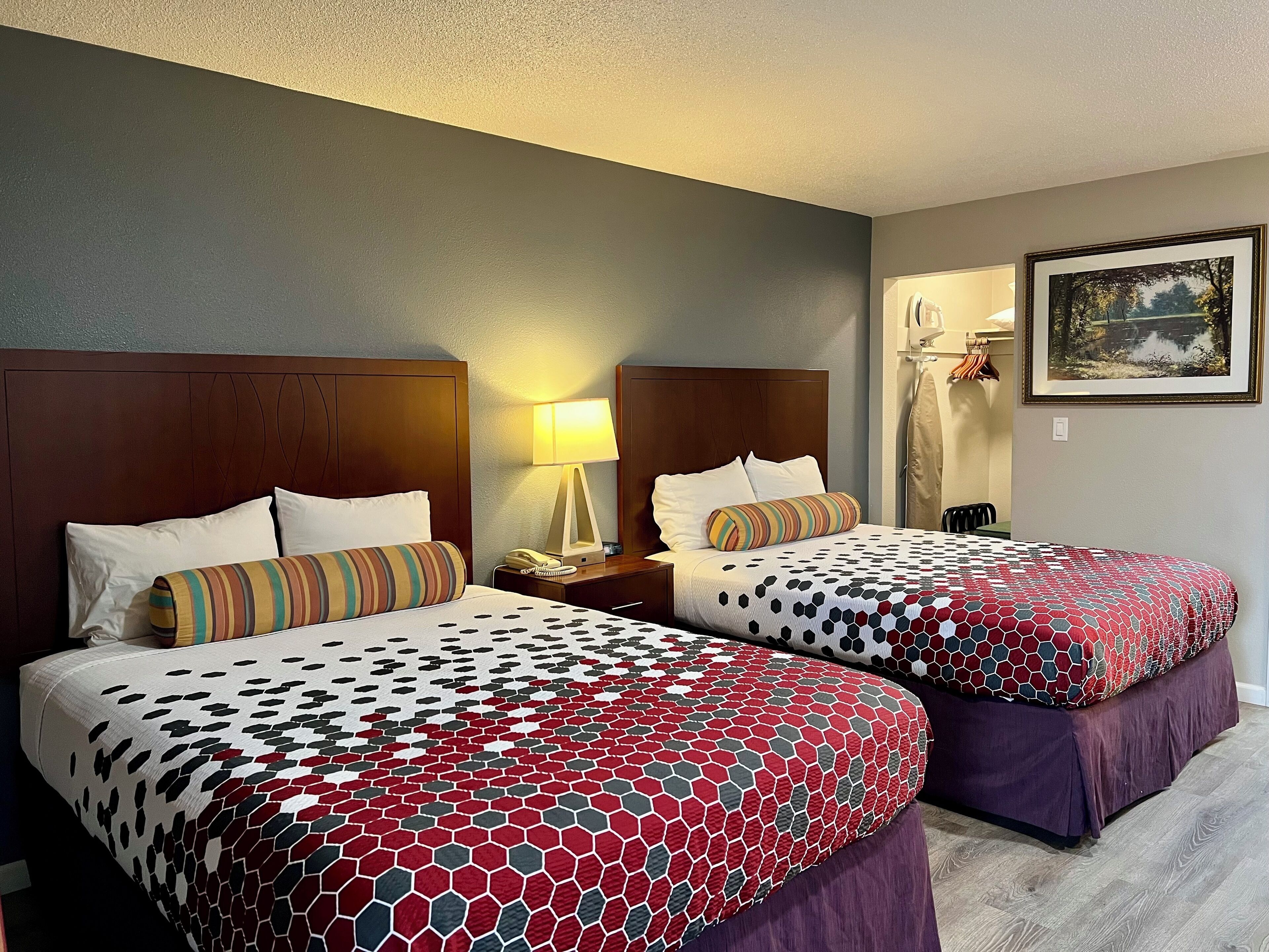 A hotel room with two beds, each with a patterned bedspread, a nightstand with a lamp, and a painting on the wall.