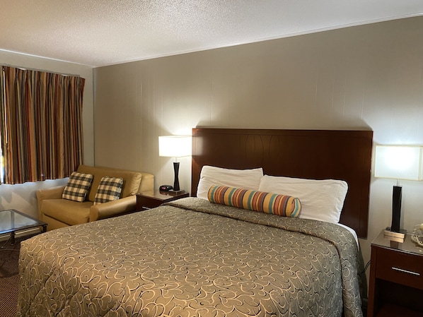 A hotel room with a large bed, a sofa, two lamps, a nightstand, and a window with curtains.