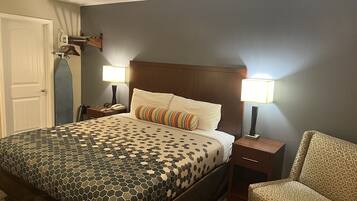 Una habitación de hotel con una cama grande, dos mesitas de noche, una silla y una puerta.
