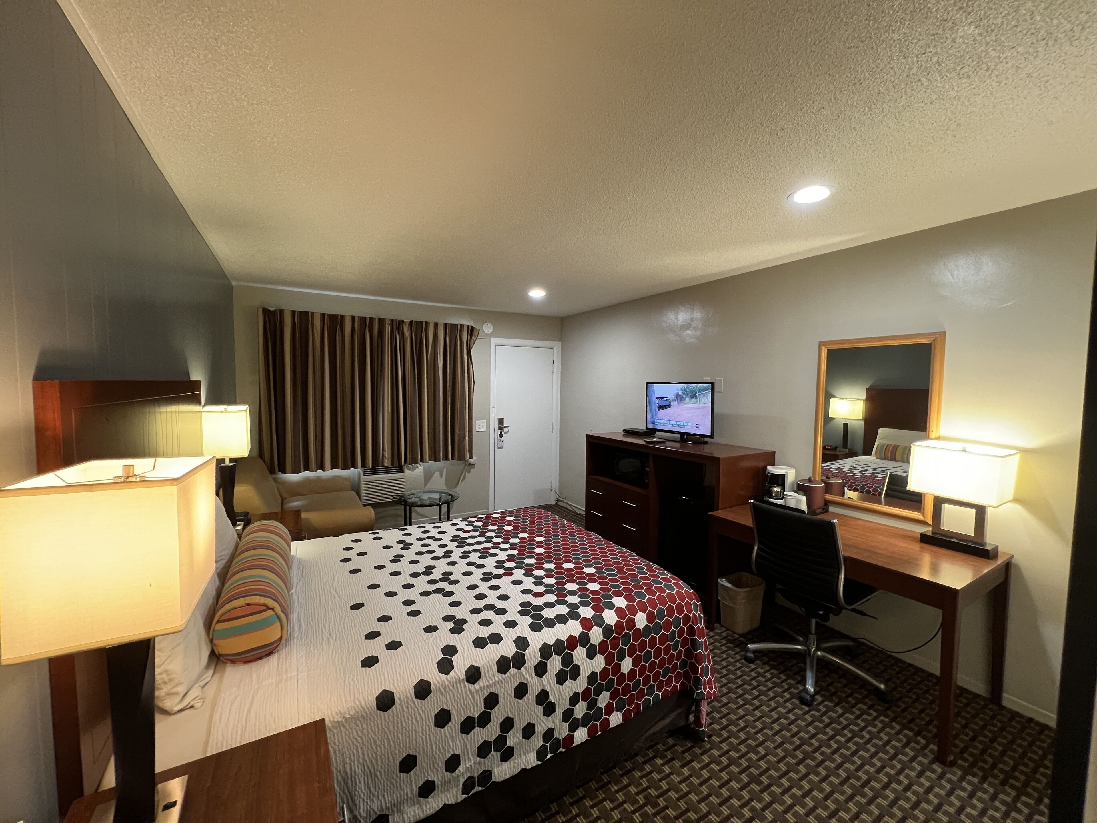 A hotel room with a bed, desk, chair, TV, and two lamps.
