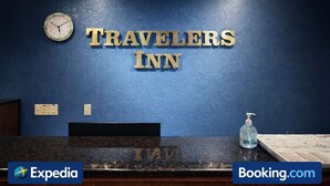Vastaanottotiski, jossa on kello, kyltti, jossa lukee ”TRAVELERS INN”, ja käsidesipannostin.