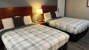 Hotellihuone, jossa on kaksi sänkyä, joissa kummassakin on ruutukuviollinen peitto, yöpöytä lampun kanssa ja ovi, jossa on kahva.