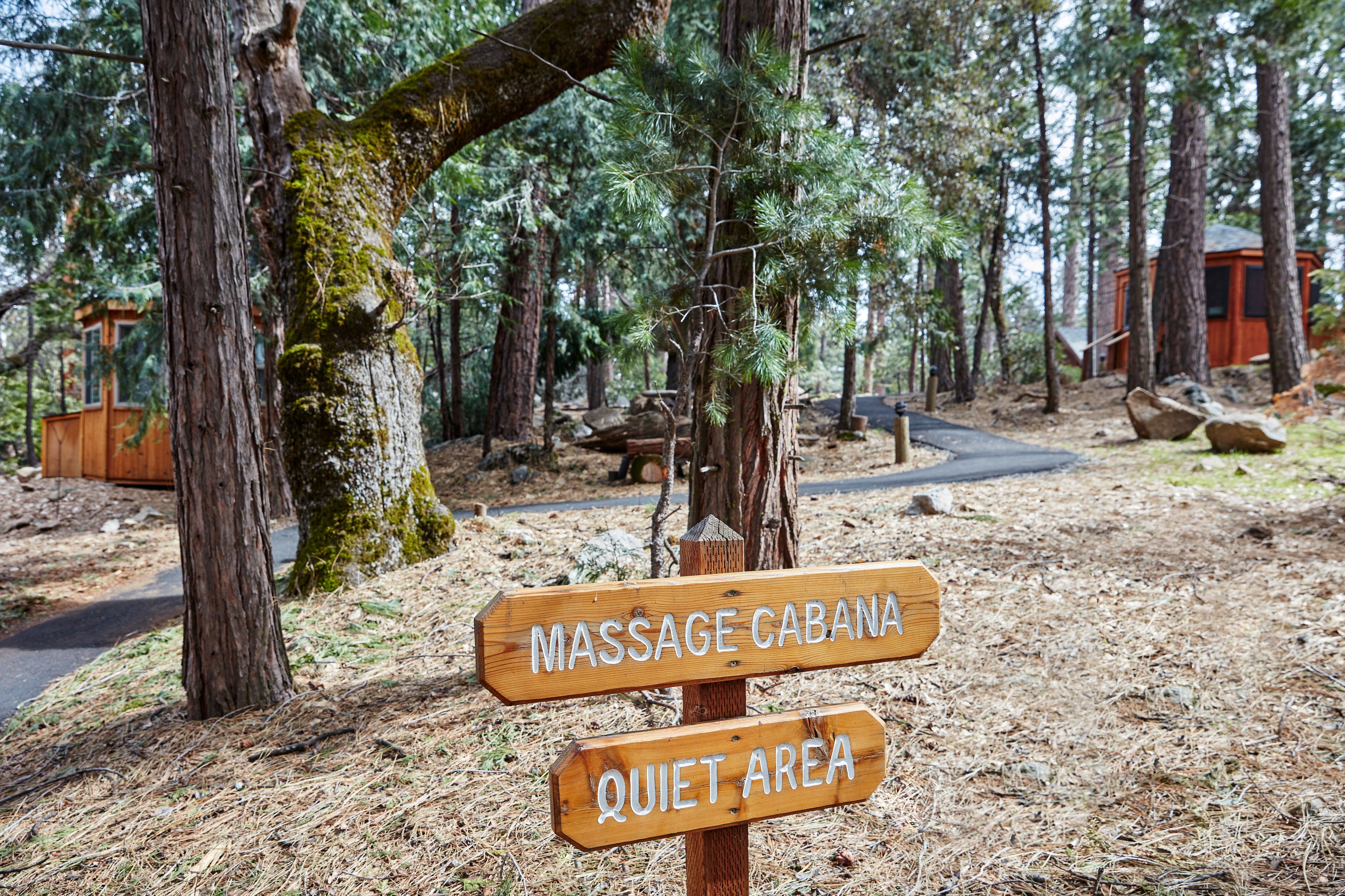 A wooden signpost in a forested area with 'MASSAGE CABANA' and 'QUIET AREA' written on it.