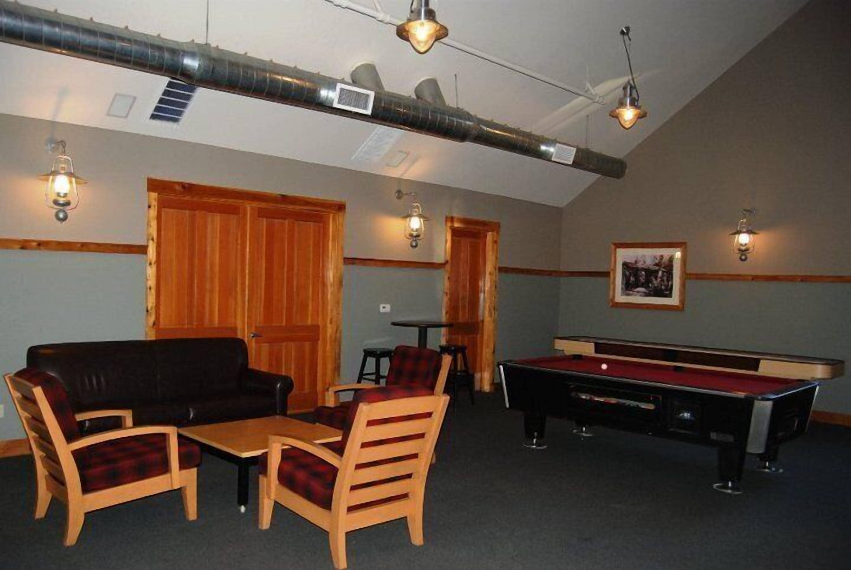 A room with a pool table, a sofa, and two chairs. There are wooden doors and a framed picture on the wall.