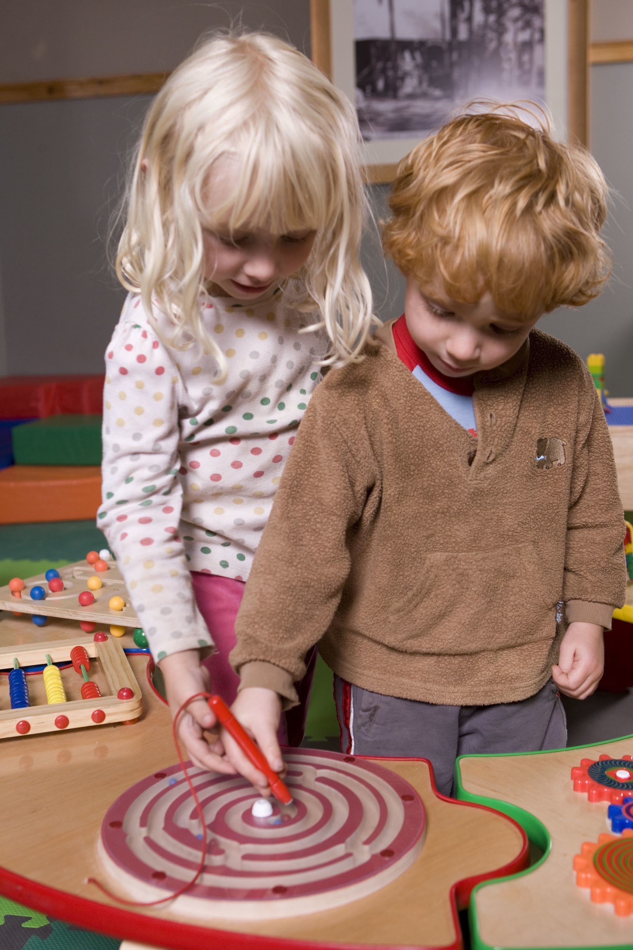 Two children playing with a wooden puzzle and a spinning top.