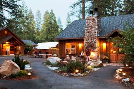A lodge with a stone chimney, wooden exterior, and a paved entrance with outdoor seating.