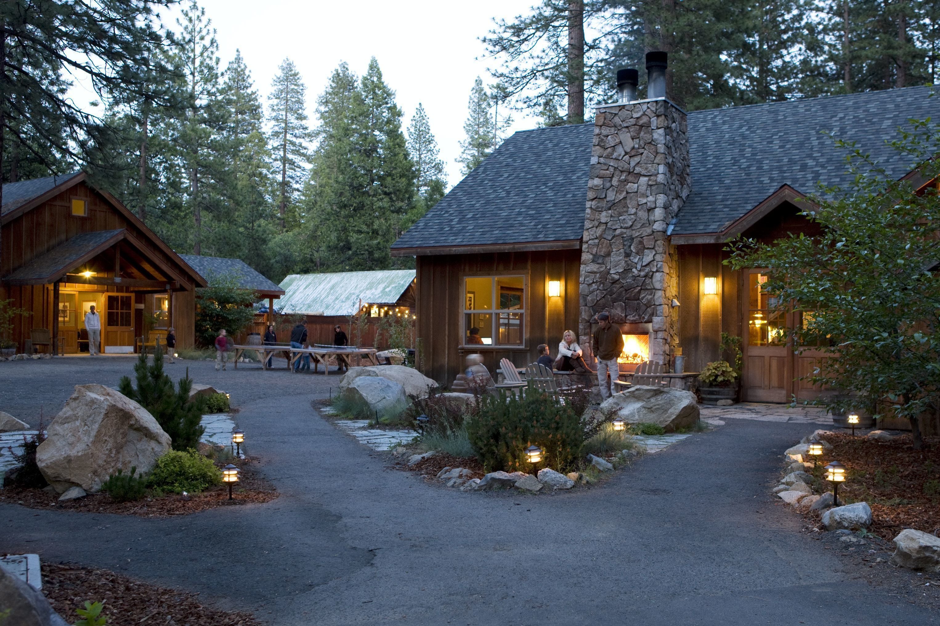 A lodge with a stone chimney, wooden exterior, and a paved driveway with outdoor seating.