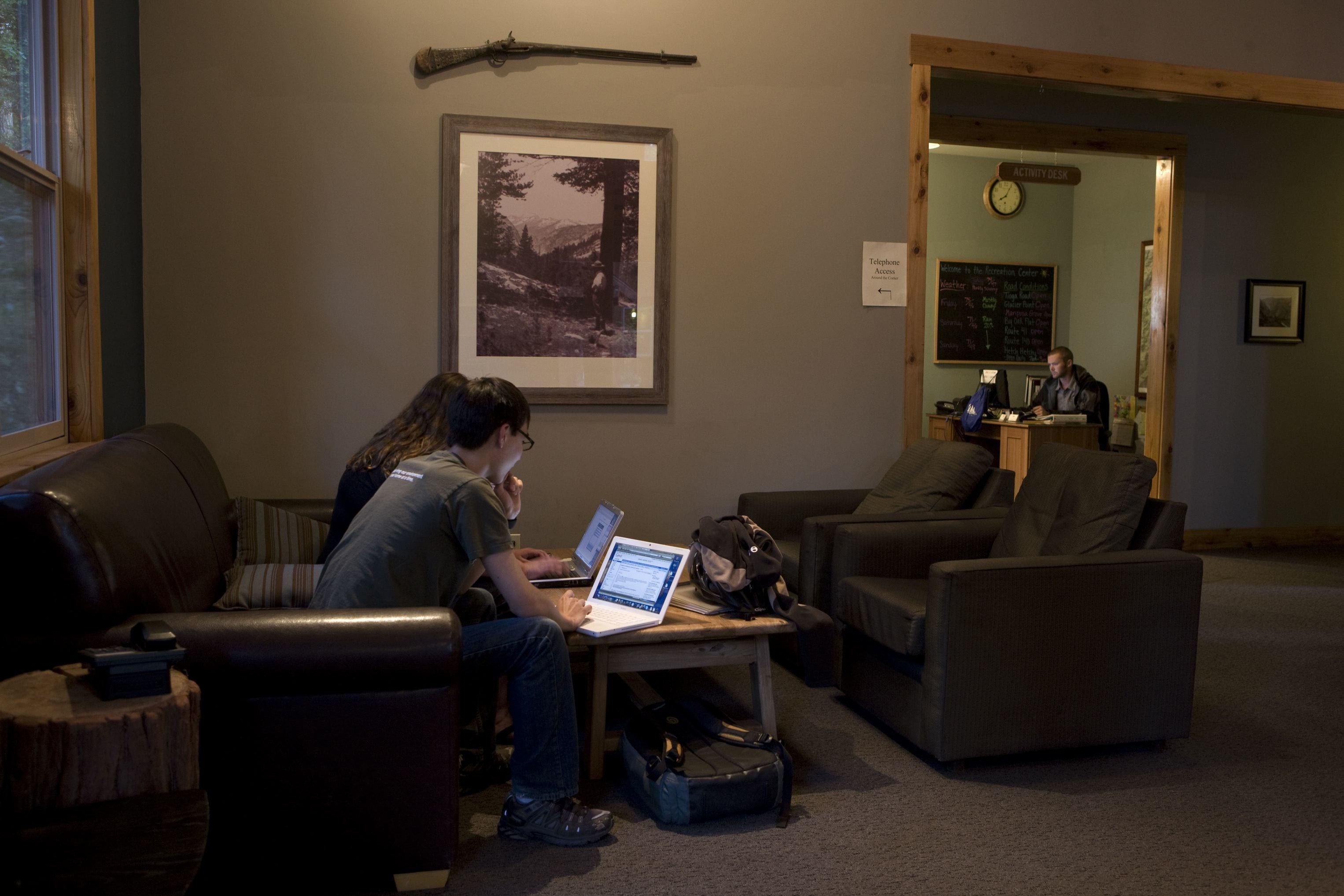 A room with a desk, two chairs, a laptop, and a framed picture on the wall.