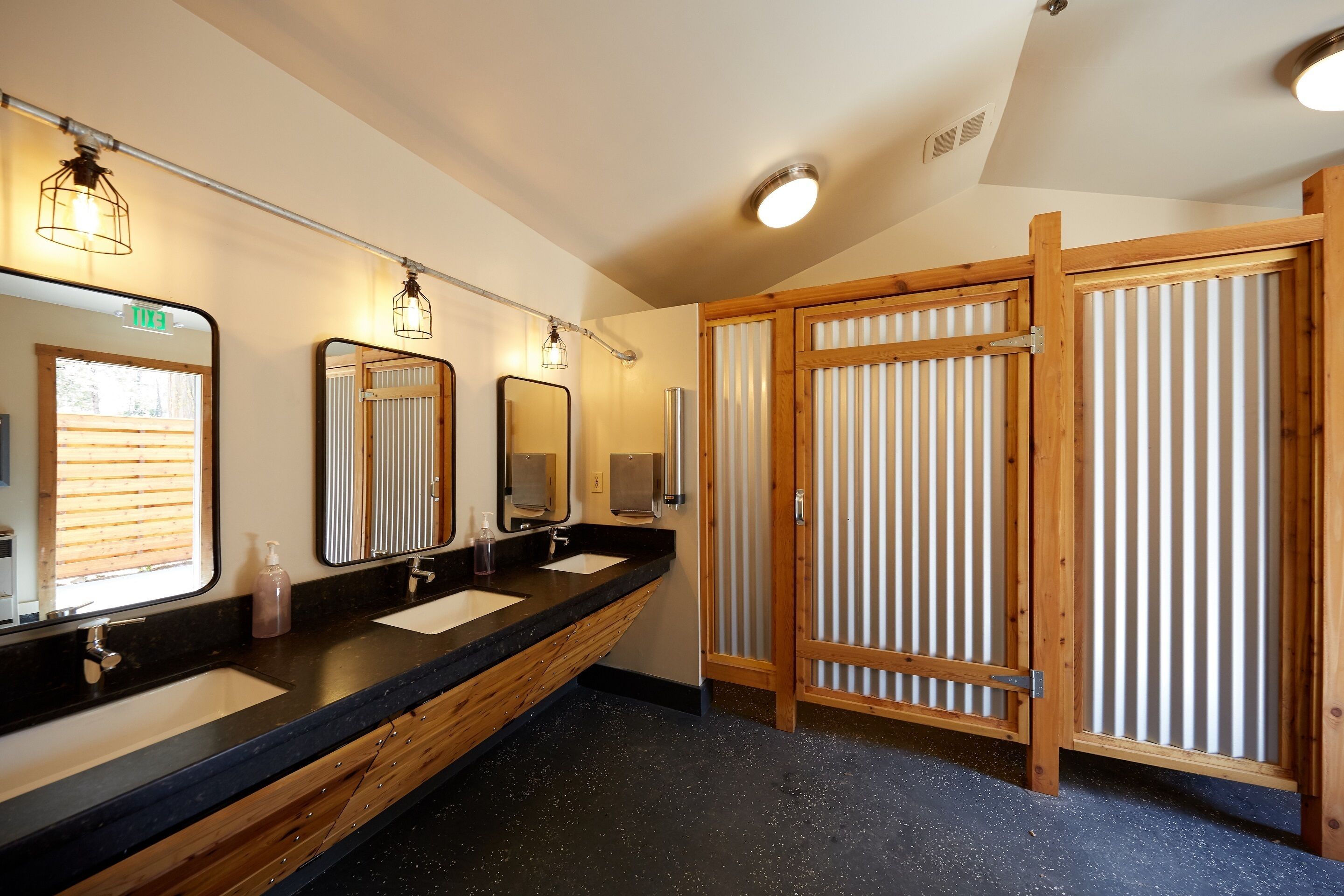 A modern bathroom with three sinks, wooden cabinets, and a large mirror.