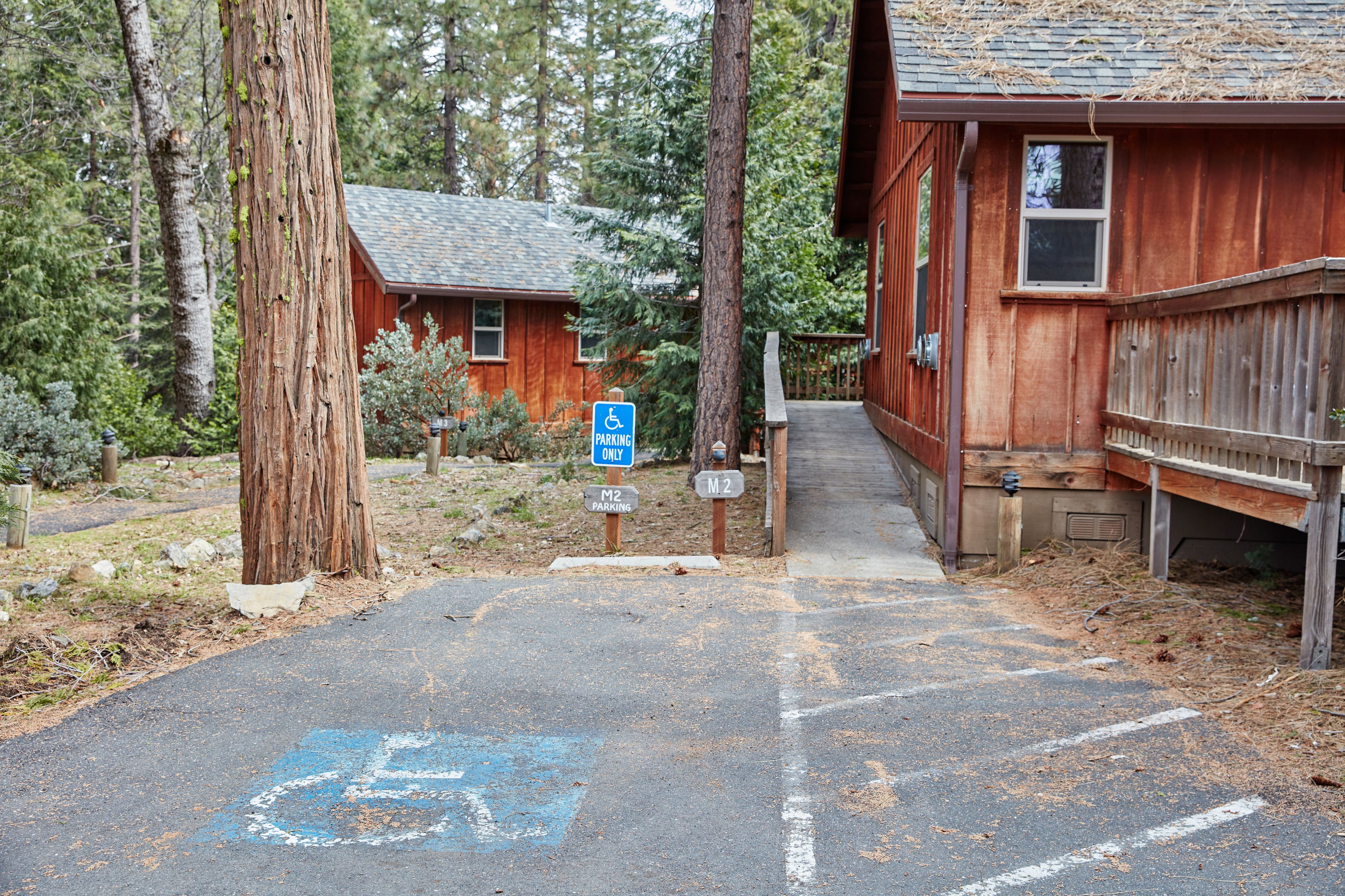 A wooden cabin with a wheelchair-accessible parking area and a covered walkway leading to the entrance.
