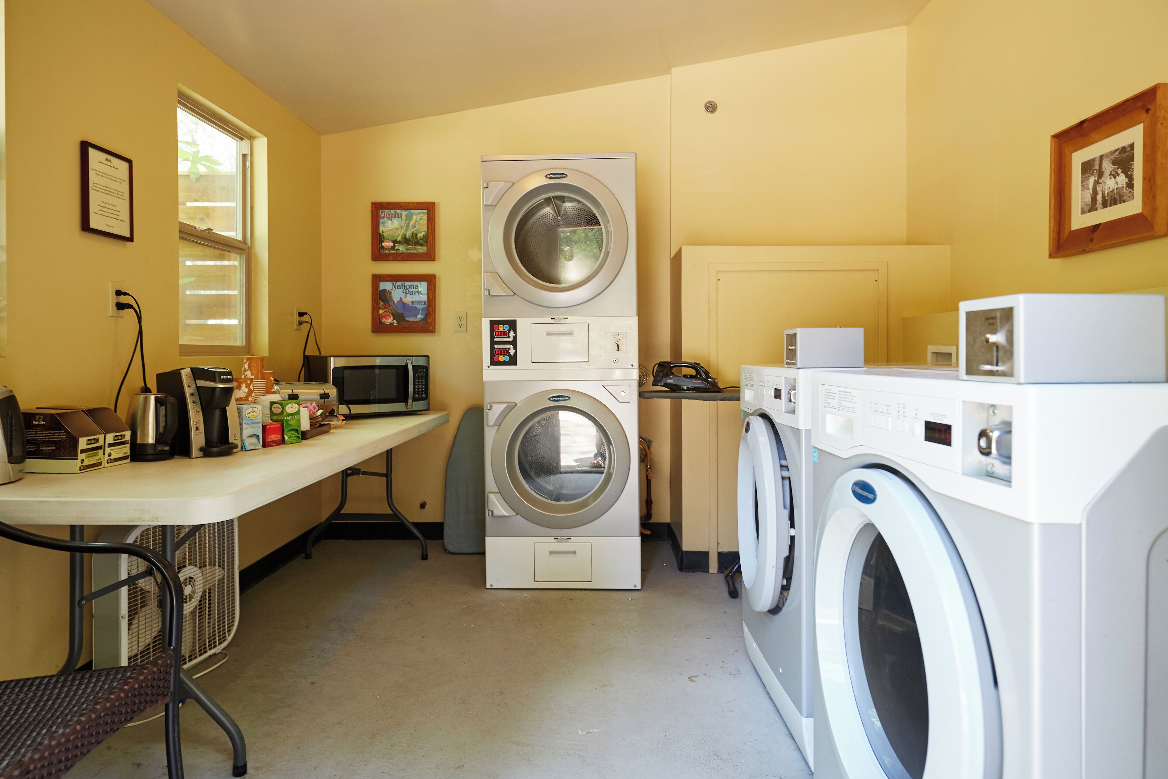 A laundry room with two stacked washers and dryers, a microwave, and a table with various items.