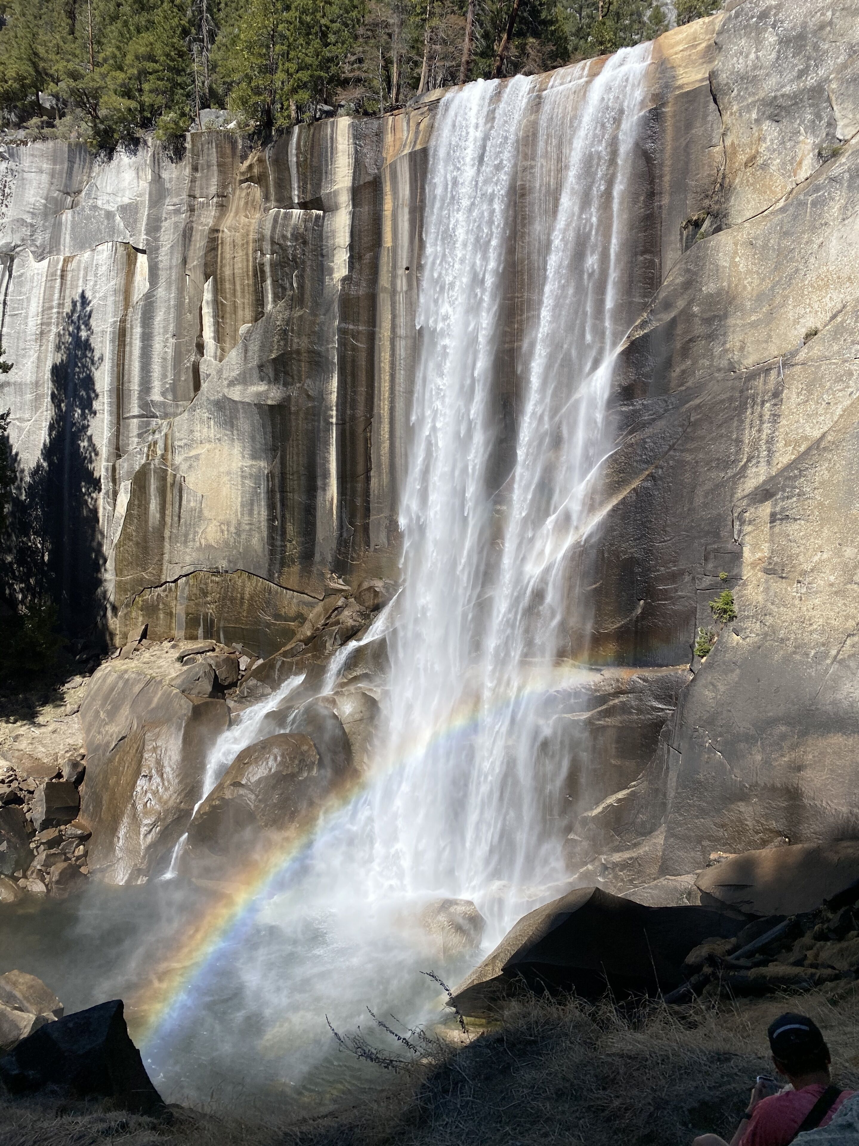 A waterfall cascading down a rocky cliff with a visible rainbow at the base.