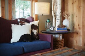 A cozy room with a blue sofa, a lamp, a small table with a clock, and a birch tree.