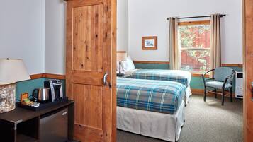 Een hotelkamer met een houten garderobe, een bed met een ruitdessin dekbedovertrek, een stoel, een bureau met een lamp en een koffiezetapparaat.