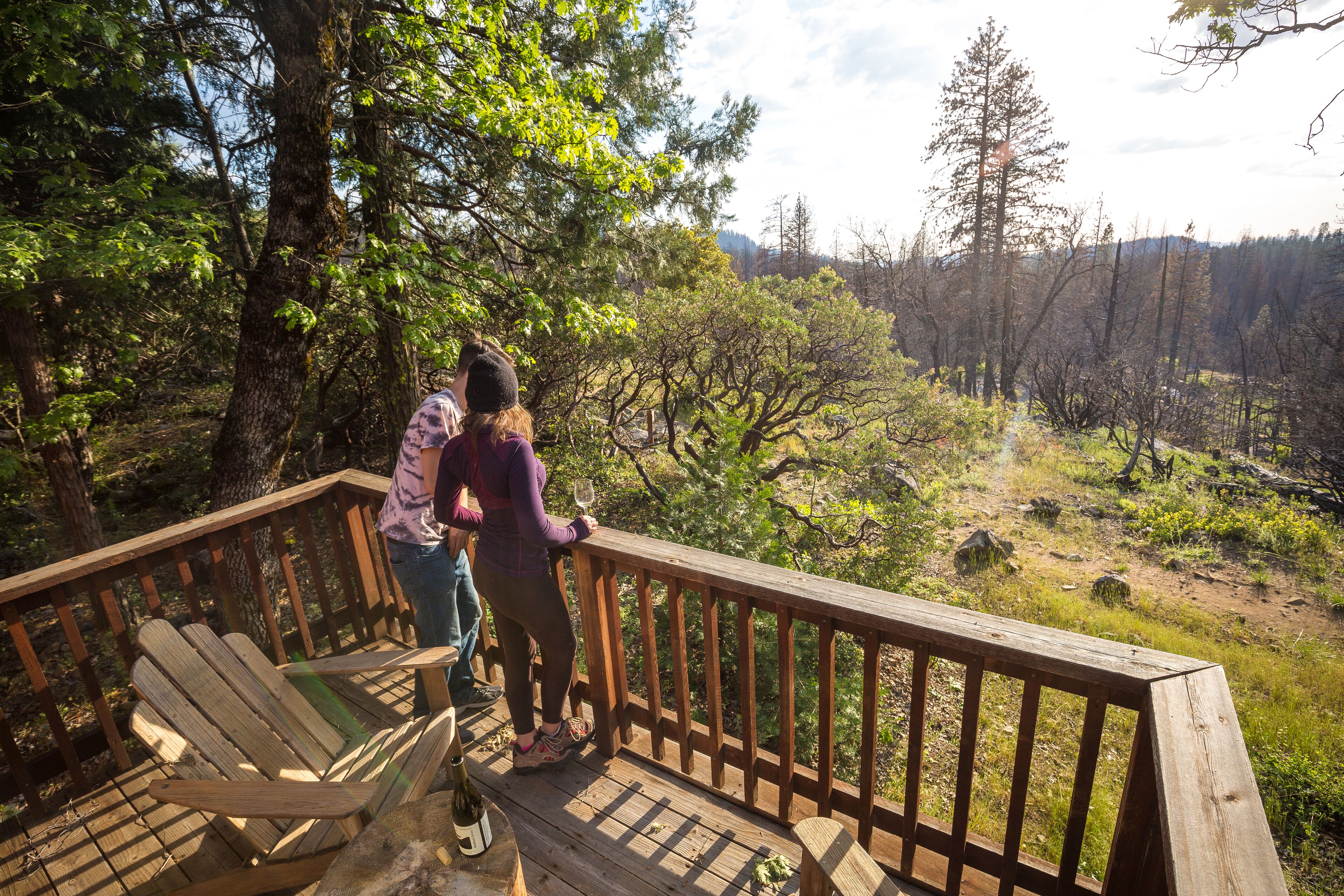 A wooden deck with a chair and a railing overlooking a forested area.
