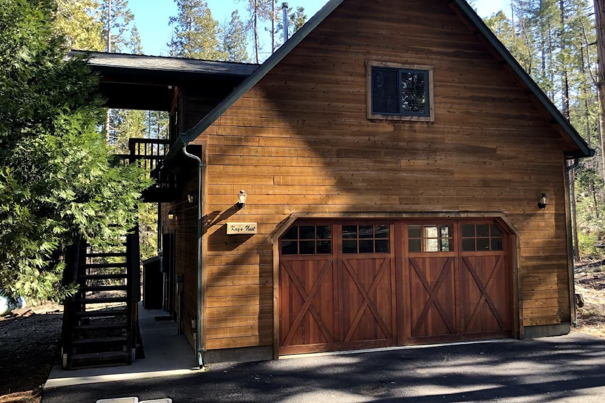 A wooden cabin with a garage, a covered porch, and a sign reading "Kay's Nest".