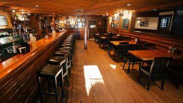 A bar area with wooden floors, bar stools, and a counter with various bottles and glasses.