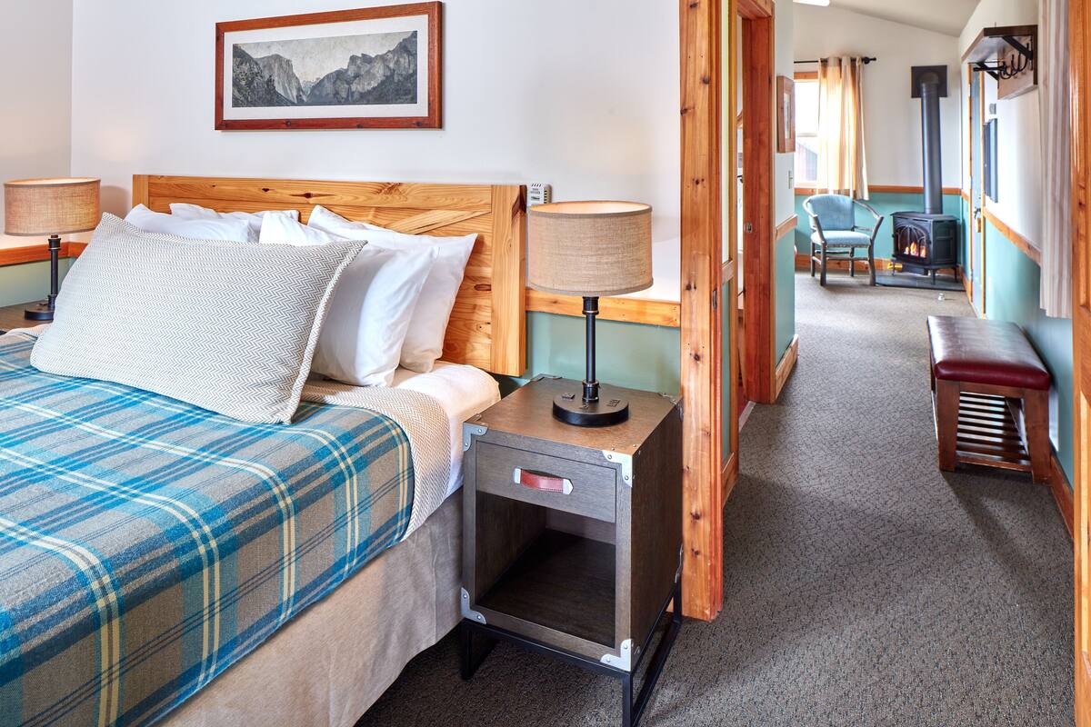 A hotel room with a bed, bedside tables, a chair, a bench, a fireplace, and a framed picture on the wall.