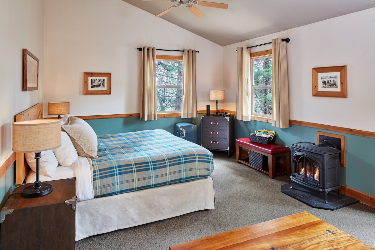A cozy room with a bed, a wooden bench, a dresser, and a wood-burning stove.