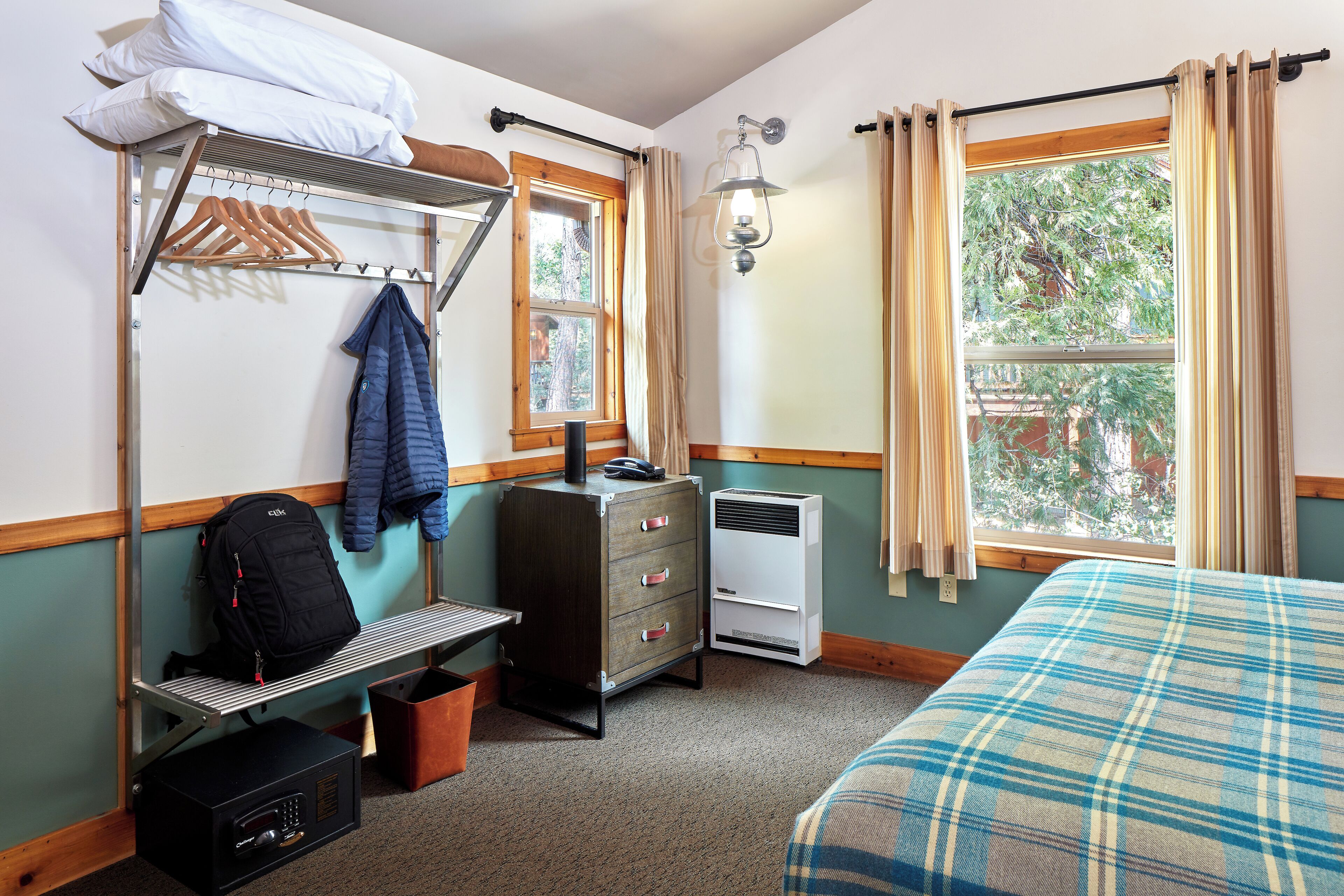 A room with a bed, a bench, a wardrobe with hanging clothes, a heater, and a window with curtains.
