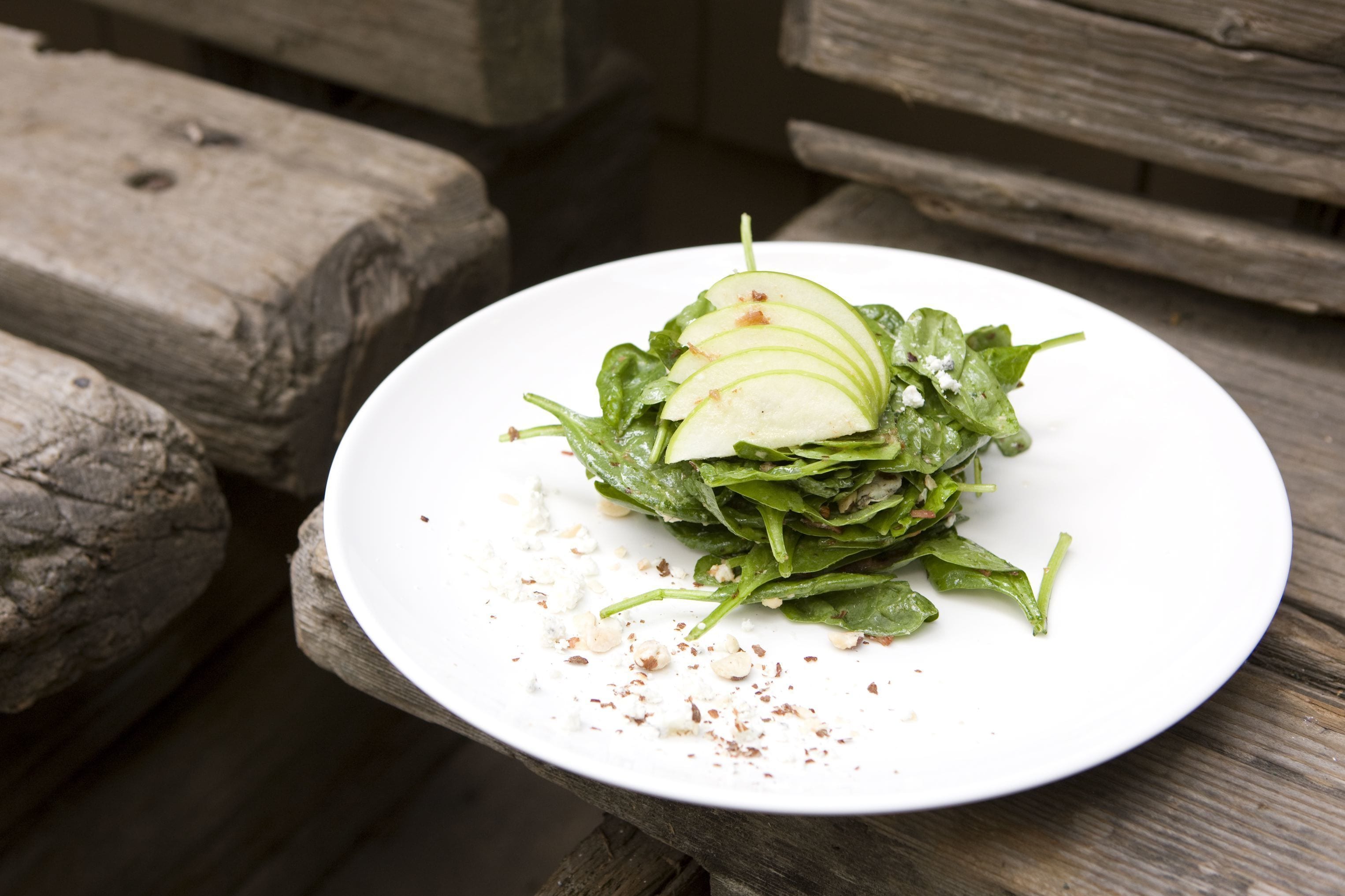 A white plate with a salad on a wooden table.