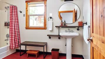 Un baño con un banco de madera, un lavamanos, un espejo y una cortina de ducha a cuadros rojos y blancos.