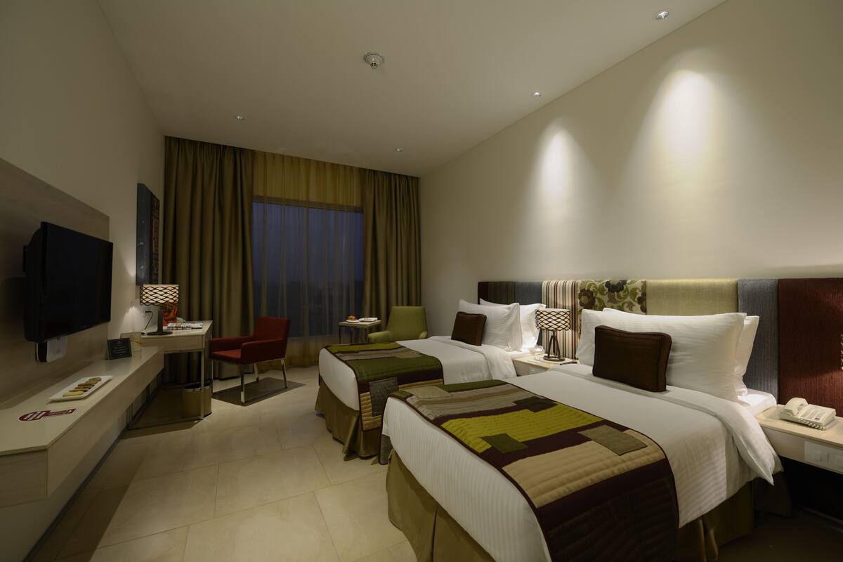 A hotel room with two beds, a desk with a computer, a TV, and a chair.