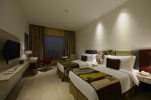 A hotel room with two beds, a desk with a computer, a TV, and a chair.