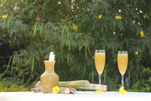 A table with two glasses of a yellow beverage, a bottle, and some ginger slices.