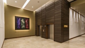A modern hotel lobby with a large abstract art piece on the wall, a reception desk, and a sign indicating the name 'MARATHA'.