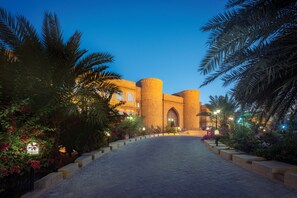 A grand building with a large arched entrance, surrounded by a paved walkway and lush greenery.