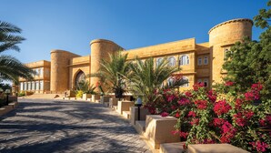 A large building with a grand entrance, featuring a paved pathway leading to the main entrance, surrounded by palm trees and flowering plants. - Rang Mahal Jaisalmer (Jaisalmer)