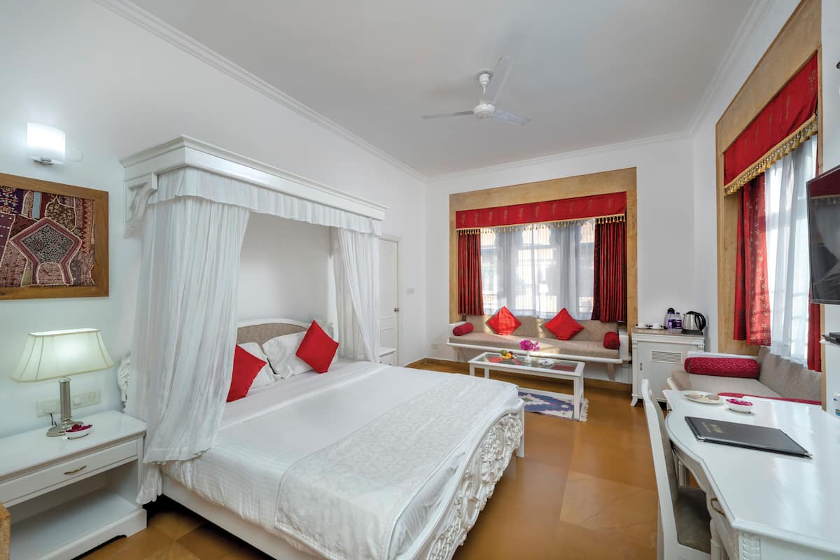 Un dormitorio amplio con cama con dosel, zona de estar con sofá y sillones, y escritorio con silla.