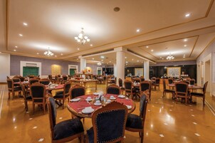 Un amplio salón de banquetes con varias mesas redondas y sillas, candelabros elegantes y un piso de madera pulida.