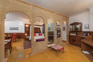 A room with a bed, a desk, a chair, a small table, and a cabinet.