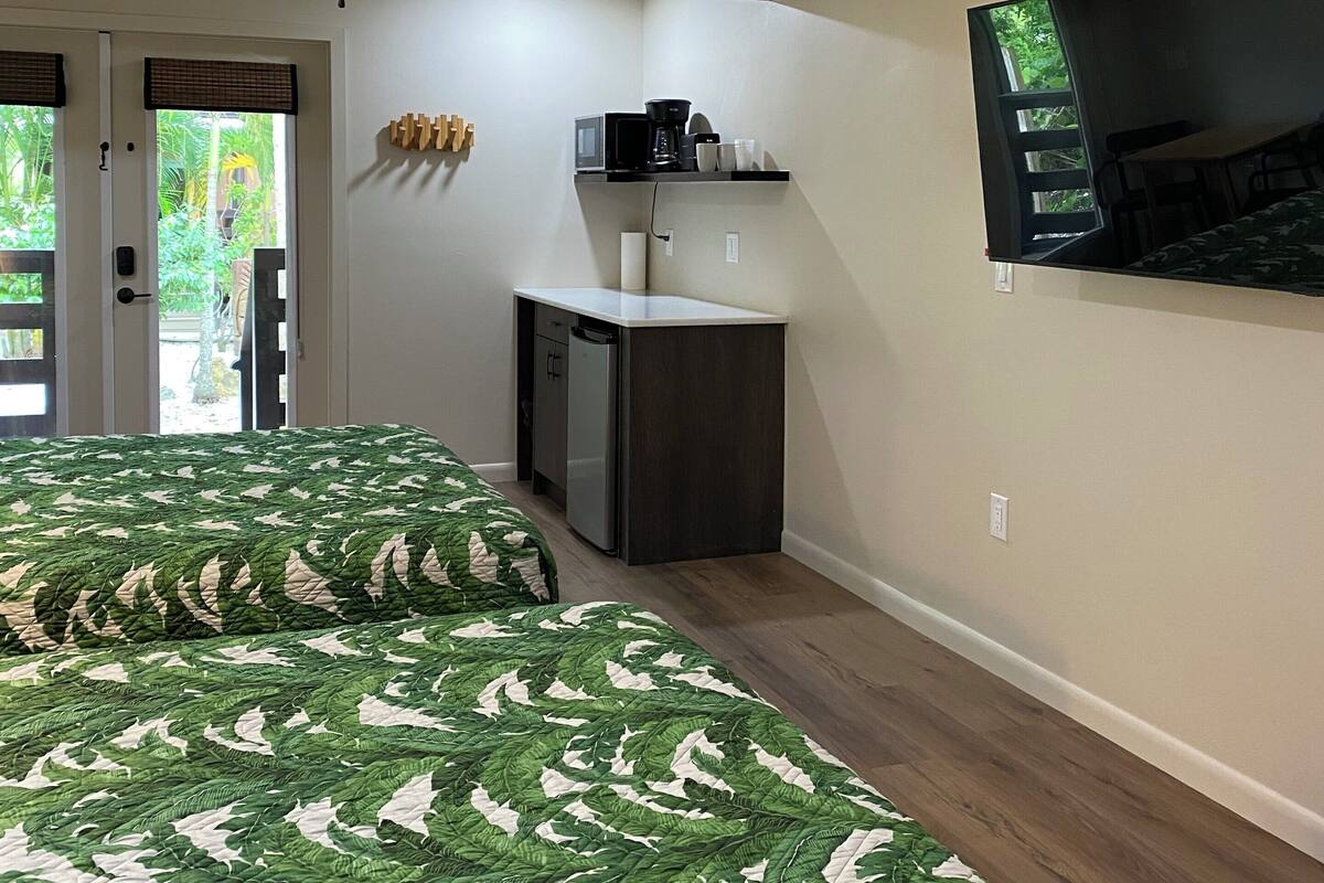 Ein Schlafzimmer mit Bett, einer kleinen Küchenzeile, einem Deckenventilator und einem an der Wand montierten Fernseher.