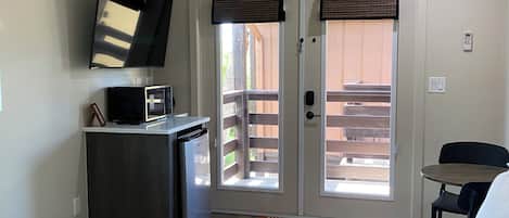 A bedroom with a bed, a ceiling fan, a desk with a computer, a TV, and a door leading to a balcony.