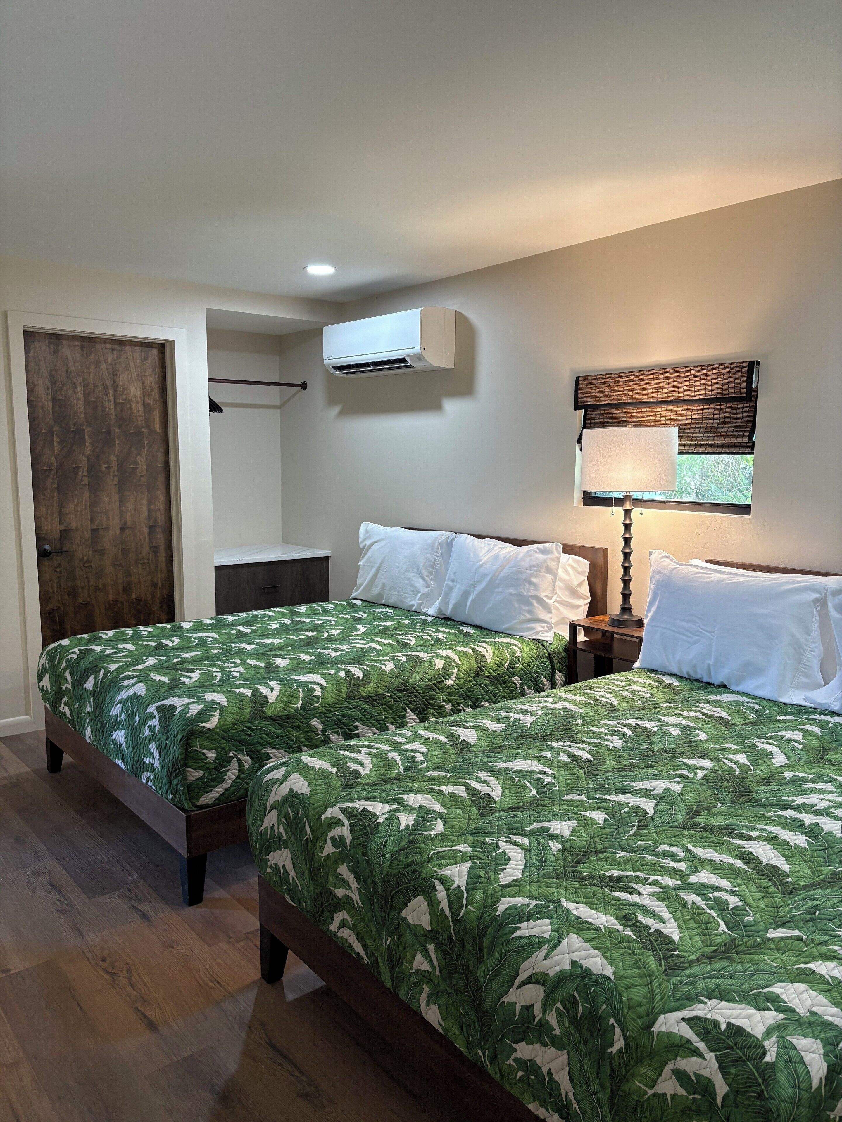 Un dormitorio con dos camas, una ventana con vistas, un aire acondicionado y una lámpara de noche.