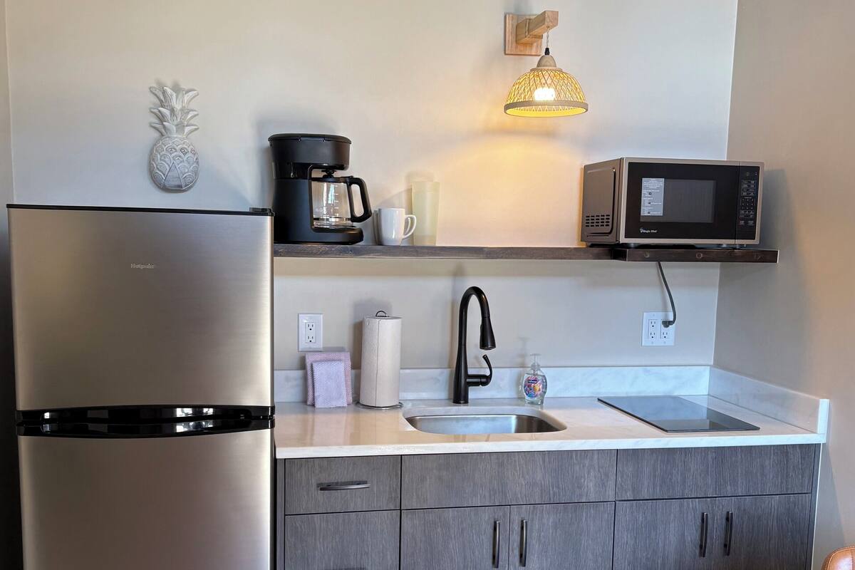 Eine kompakte Küche mit einem Edelstahlkühlschrank, einer Mikrowelle, einer Kaffeemaschine und einem Spülbecken.