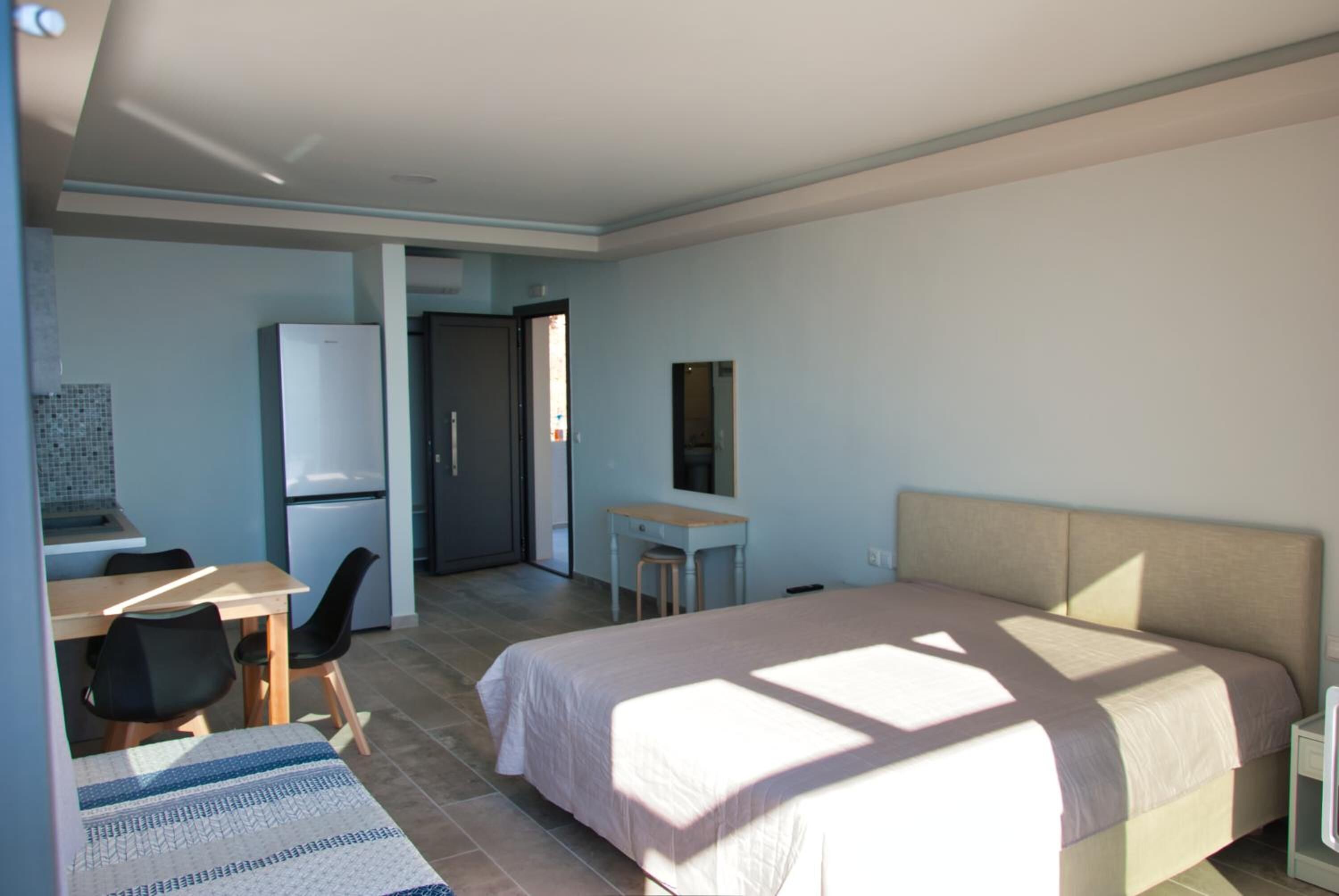 Een moderne hotelkamer met een bed, een bureau, een stoel, een klein tafeltje en een koelkast.