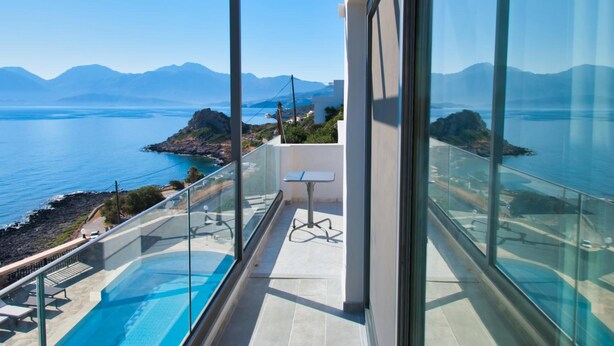 A balcony with a glass railing overlooking a body of water and distant mountains.