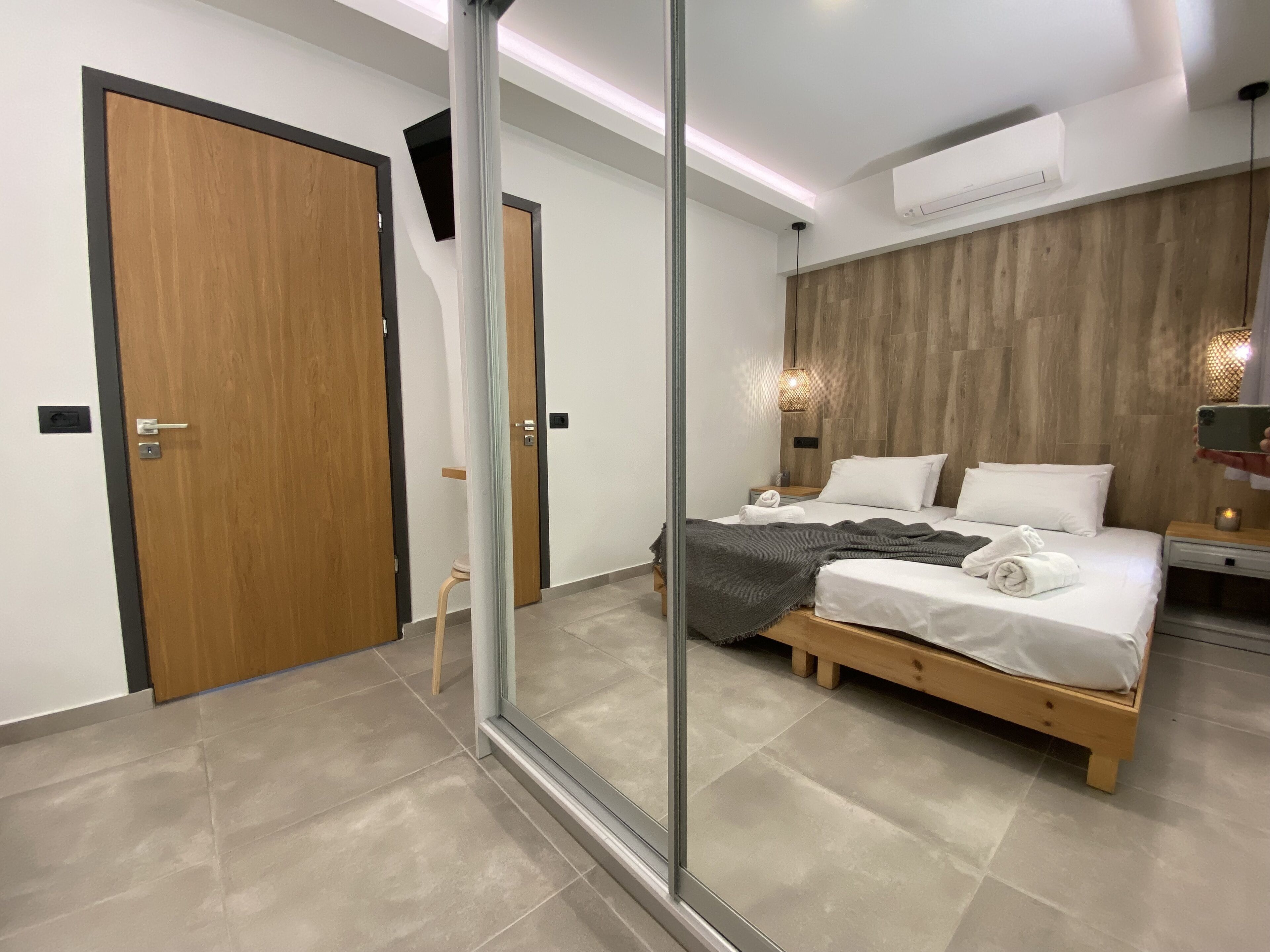 A modern bedroom with a wooden bed, a nightstand, and a mirror reflecting the room.